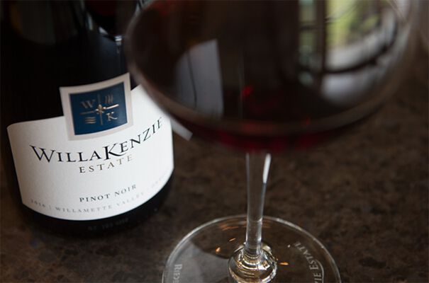A close up  on the label of a WillaKenzie Estate wine bottle with a glass of red wine standing next to it.
