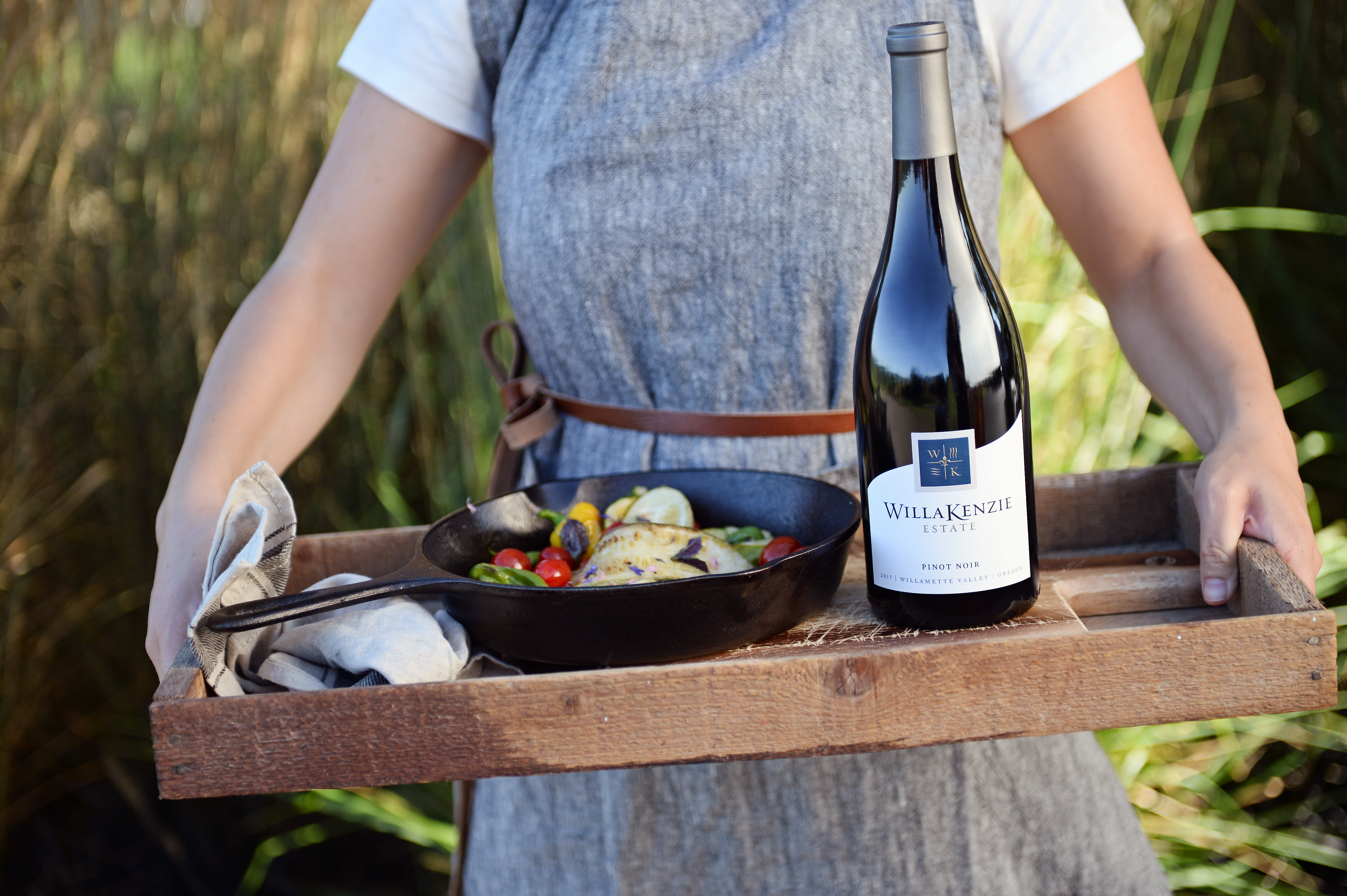 Person holding a tray with barbecued food and a bottle of WillaKenzie wine.